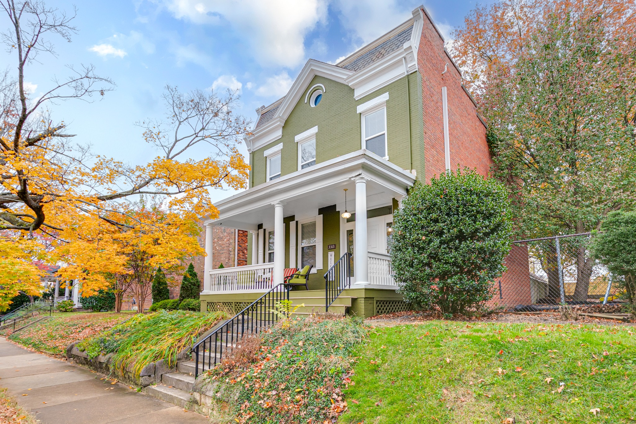 Green Richmond home with a white porch and autumn trees